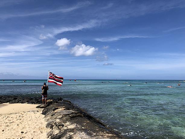 海に向かってハワイの州旗を持っている男性。