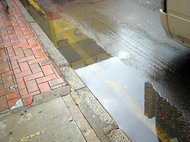 水の溜まる道路。狭い香港、車が通過して水が撥ねるので注意が必要です。