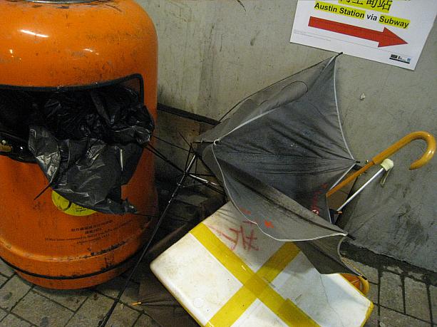 ゴミ箱に捨てられた傘が、台風による風が強いことを物語っています。