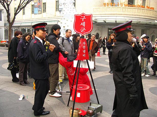 あっ、これは救世軍の慈善鍋！日本では社会鍋と言うそうですね。<br>街頭で募金運動をする救世軍。毎年この時期に登場します。<br>ん？真っ赤なお鍋の前に、何だか小さな人が・・・！？