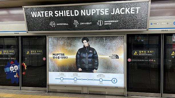 冬は寒い日が続く韓国だけに防寒着は必需品。ダウンジャケットで人気のノースフェイスは日本でもおなじみでしょう。地上に上がるときに利用されやすい西側の階段のもっとも近い位置に出ている広告です。モデルは超イケメンのチャ・ウヌ。