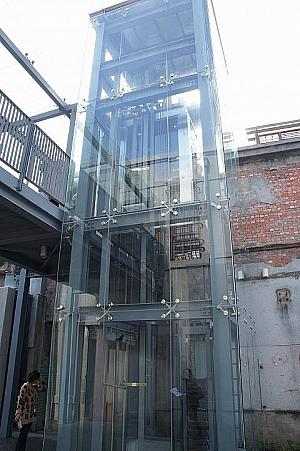 オフィスは2F、モダンな透明のエレベーターを古い建物の横に設置して、ここにも古さとの上手いコントラスト