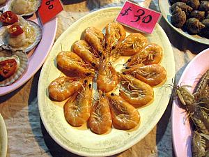 ■ 「白灼蝦（パクチョハー・塩茹で蝦）」<br>
香港式海鮮の定番メニューと言えばこれ。蝦を塩茹でしただけのシンプルな調理法ですが、茹でたての蝦の殻をはずして、唐辛子入りの醤油ダレにつけて食べるその味は、まさに、香港に来てよかった～、と実感するはず。豪快に手でパクリといただくこの料理、誰もが夢中になって食べてしまうおいしさです。おいしさの秘密は、直前まで生きていた新鮮な蝦をさっとゆでることにあります。新鮮なものはシンプルにその素材の味を楽しむものなのですね。これは、前菜的な位置づけですので、最初にオーダーするのがベスト。手を使って食べるため、小さなボウルにお茶を入れた、フィンガーボールをもらって手を洗うことができます。また他に蝦をニンニクでさっと揚げたメニューもあります。