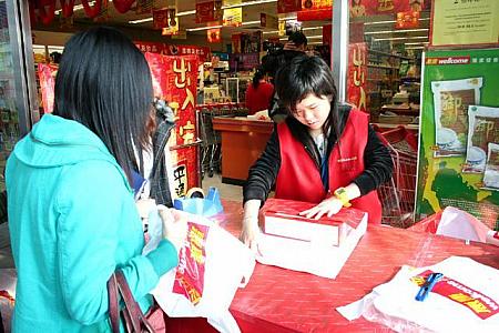 このウエルカムの入り口には、店員のお姉さんが立っています。これは、プレゼント用に買った品物を、赤い包み紙で包装してくれる特設コーナーなんです。こんなふうに、手際よく、包装してくれます。そう、香港の旧正月には、縁起のよい赤は欠かせません！うっかり、白い包装を渡してしまった日には、えらいことになっちゃいますしね。 （ナビ注：香港では、白は縁起が悪い色なんです）