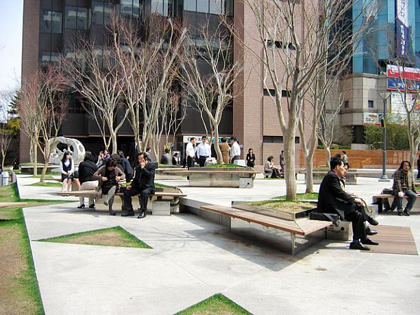お昼休みも終了間際の午後1時頃。オフィス街の広場では、ランチを終えて昼休みの残り時間を楽しむ会社員たちがいっぱい。