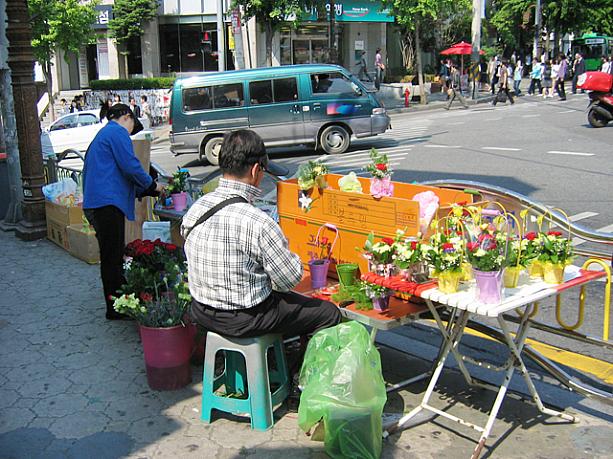 大学の正門前の交差点。いつもはないのに、今日は花かごの出店が！？オボイナル（父母の日）はちょうど先週終わったトコだけど・・・？