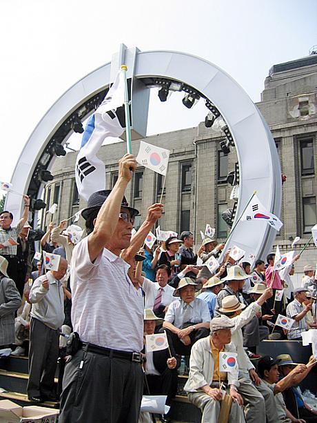 集まった人たちは太極旗を掲げてデモの演説に賛同しています。ところで市庁舎の時計が無いのはなぜ？