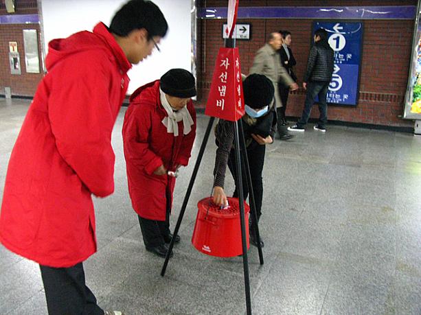 この赤いバケツみたいなのが、韓国語では「チャソンネンビ」、訳して「慈善鍋」と呼ばれる募金箱。通りすがりに募金をしていく人、結構いるんですョ！