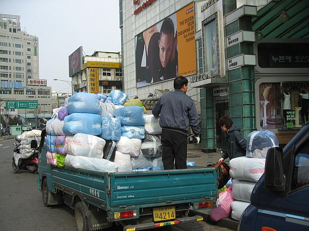実は、この袋の中身は衣料品。卸の商品がたくさんどこかに運び出されているところだったんですね～。確かに衣料品だと、しっかりとした箱に入れなくても大丈夫だし、こんなビニール袋のほうが少しでも重量が軽くて大量に運ぶのにはいいかも。