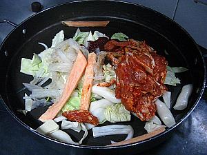 １．油をしいた鉄板に切った野菜と戻した餅などの具、下味を付けておいた鶏肉、残りのヤンニョム（薬味）をのせ、