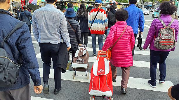 秋深まり冬の足音が聞こえてきた最近、何か美味しいものが食べたくなると市場に自然と足が向かってしまいます。行き先はソウルで最も安いと名高い、京東市場です。こうやって車輪のついたバッグを転がすご婦人方を見かけるのも韓国の市場らしい風景。もう皆さん、すっかり軽めのダウンを着ています。