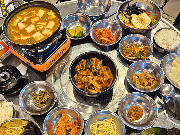 ランチタイム限定メニューの「チョングクチャン（韓国式納豆鍋）＆チェユクポックム（豚肉の甘辛炒め）」を注文したところ、、「チャプチェ」、「コサリナムル（わらびの和え物）」、「ムグンジポックム（炒めた熟成キムチ）」、「コンナムルムッチム（大豆もやしの和え物）」、「ムセンチェ（大根の和え物）」、「ホバクムッチム（カボチャの和え物）」、「おでんポックム（炒め）」など多くのパンチャン（おかず）が登場し、、何とさらにビビンバまで！