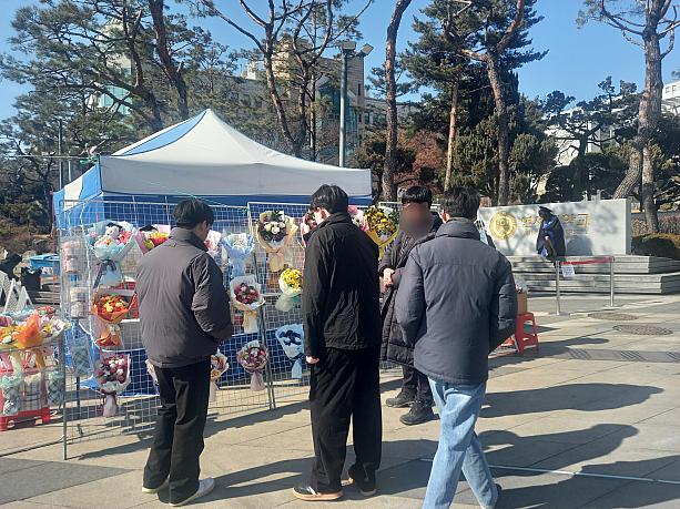 大学の正門前には花束のお店も登場~。「どれにしよっかな~？」。お友達のお祝いでしょうか？