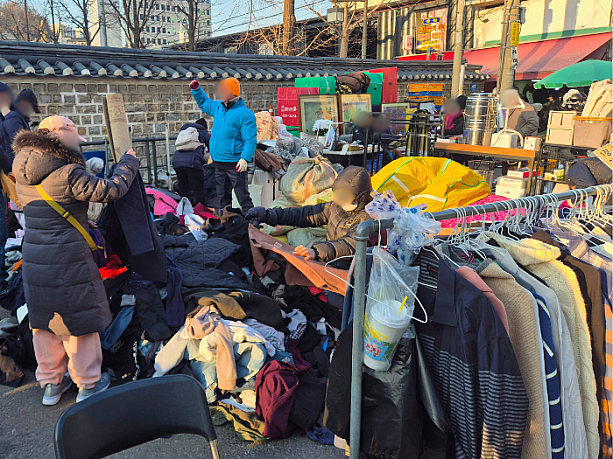 山積みにされた服が大安売りされ、品定めに余念がない人たちの様子。