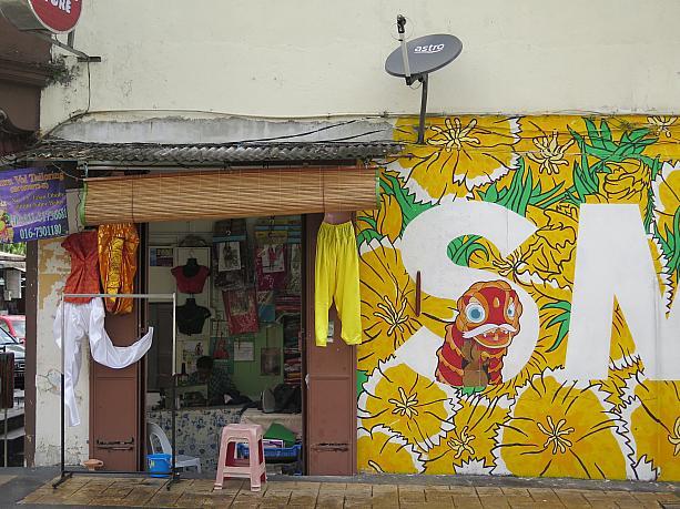 この派手な壁のあるお店の中ではインド系の女性がミシンに向かってお仕事中。