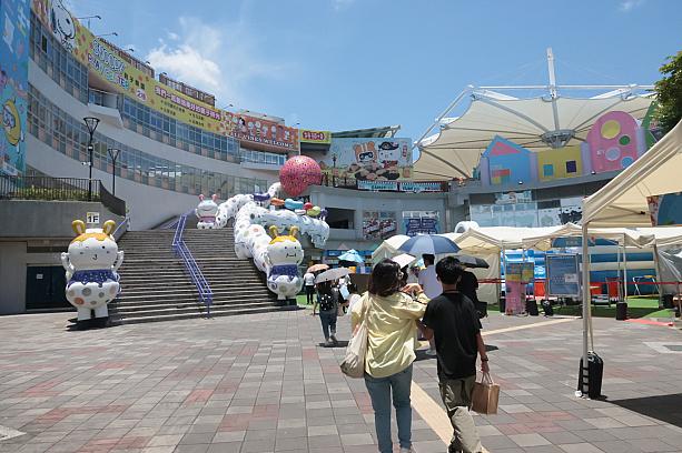 入口を通って、左へ行くと、サービスセンターや休憩施設が集まる建物があります。その前にある人工芝の広場では……