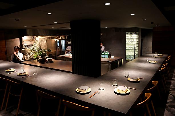 期待を胸に、2つの扉の奥へ。現れたのは落ち着いたダイニング空間です。店内の約半分をオープンキッチンが占め、それを囲むようにL字型のカウンター席(16席)が設けられています。