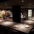 期待を胸に、2つの扉の奥へ。現れたのは落ち着いたダイニング空間です。店内の約半分をオープンキッチンが占め、それを囲むようにL字型のカウンター席(16席)が設けられています。