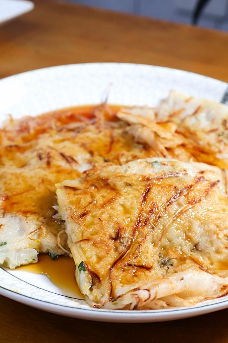 店主に聞いてみると、「阿婆粿(アーポーグイ)」は潮州でも年配の方しか知らないという料理で、起源は、忠孝路と清水路の交差点にあった新山戲院(新山映画館)の前で、一人の阿婆(お婆さん)が焼いていたことに由来すると言われています。当時、そのお婆さんは低い椅子に腰掛け、在来米(インディカ米)の米漿(米をすりつぶして作った液体)に、もやし・ニラ・九層塔(台湾バジル)を加えて焼き上げていました。この3つの食材はどれも欠かせず、ひとつでも欠けると味が変わってしまうため、「阿婆粿」には必ずもやし・ニラ・九層塔が入っています。